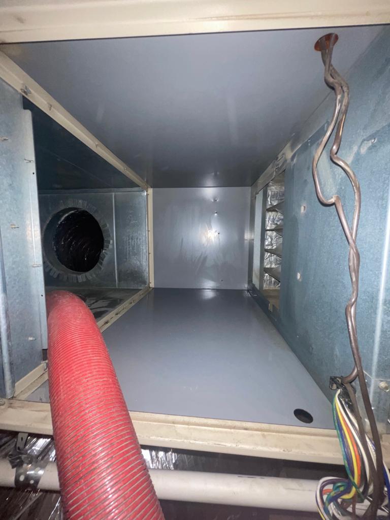 Metal duct interior and red hose setup during commercial air duct installation.