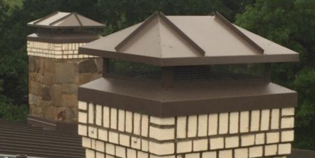 Decorative brown metal chimney caps installed on dual brick chimneys.