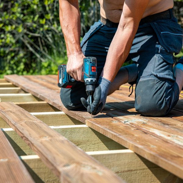 Deck construction, builder hand with electric screwdriver installing impregnated wooden boards