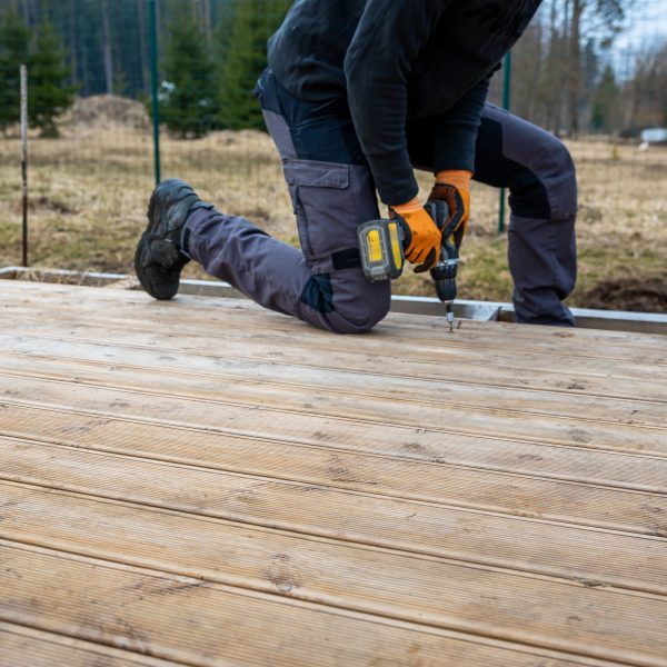 Deck or terrace construction, builder hand with electric screwdriver installing impregnated wooden boards