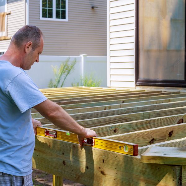 Man building a wooden patio with hammering screwing together beams close up of exterior timber decking.